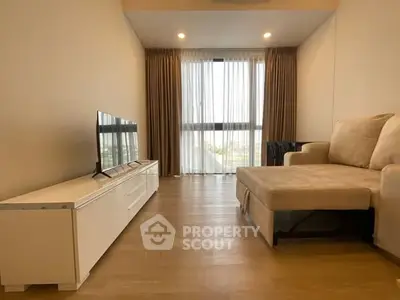 Modern living room with cozy sofa and flat-screen TV, featuring large windows and elegant curtains.