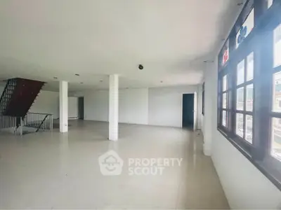 Spacious open-plan living area with large windows and staircase, ideal for modern living.