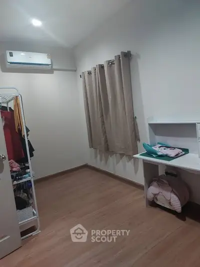 Cozy bedroom with wooden flooring, air conditioning, and ample natural light through curtains.