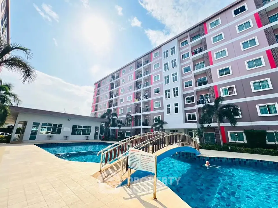 Modern apartment complex with pool and bridge under sunny sky