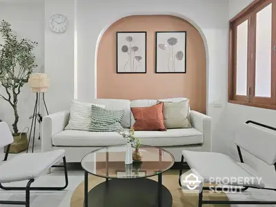 Chic modern living room with elegant white sofas, stylish glass coffee table, and charming wall art, complemented by natural light.