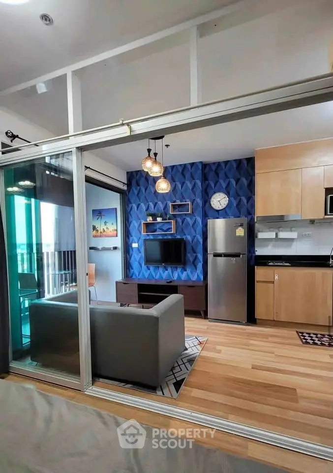 Modern open-plan living room with stylish decor and kitchen area, featuring a sleek fridge and contemporary lighting.