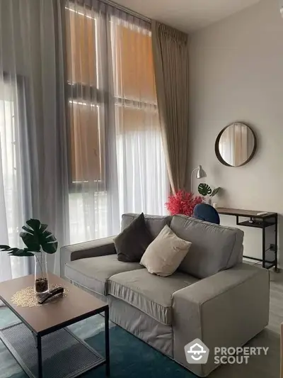 Chic modern living room with elegant gray sofa, sheer and opaque curtains, and tasteful decor, creating a serene and inviting atmosphere perfect for relaxation or entertaining guests.