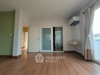 Spacious empty room with wooden flooring and large window, ideal for customization.