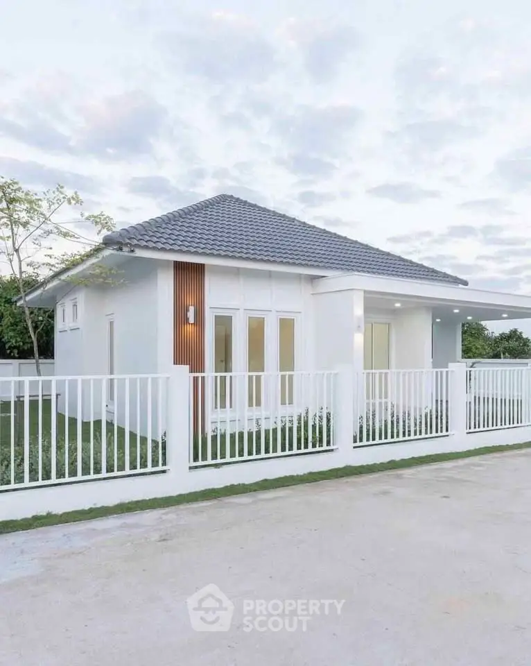 Charming modern single-story home with sleek white exterior and tiled roof, surrounded by a neat fence.