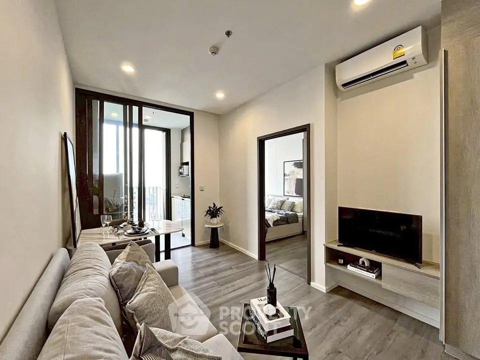 Modern living room with cozy sofa, TV, and dining area leading to a bedroom, featuring elegant decor.