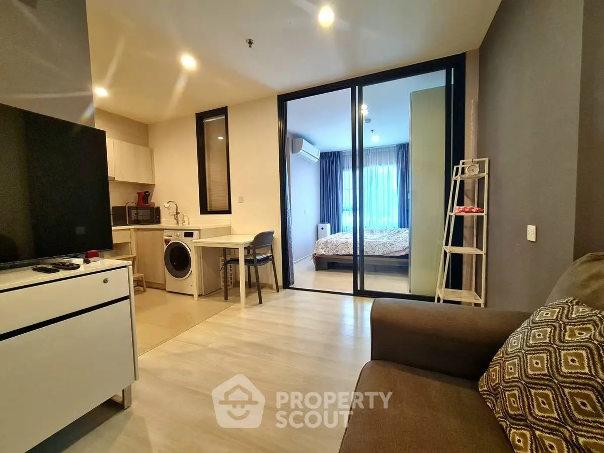 Modern studio apartment with open layout, featuring a cozy living area, compact kitchen, and bedroom with glass partition.