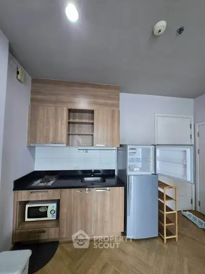 Modern kitchen with wooden cabinets, compact fridge, and built-in microwave in a cozy apartment.