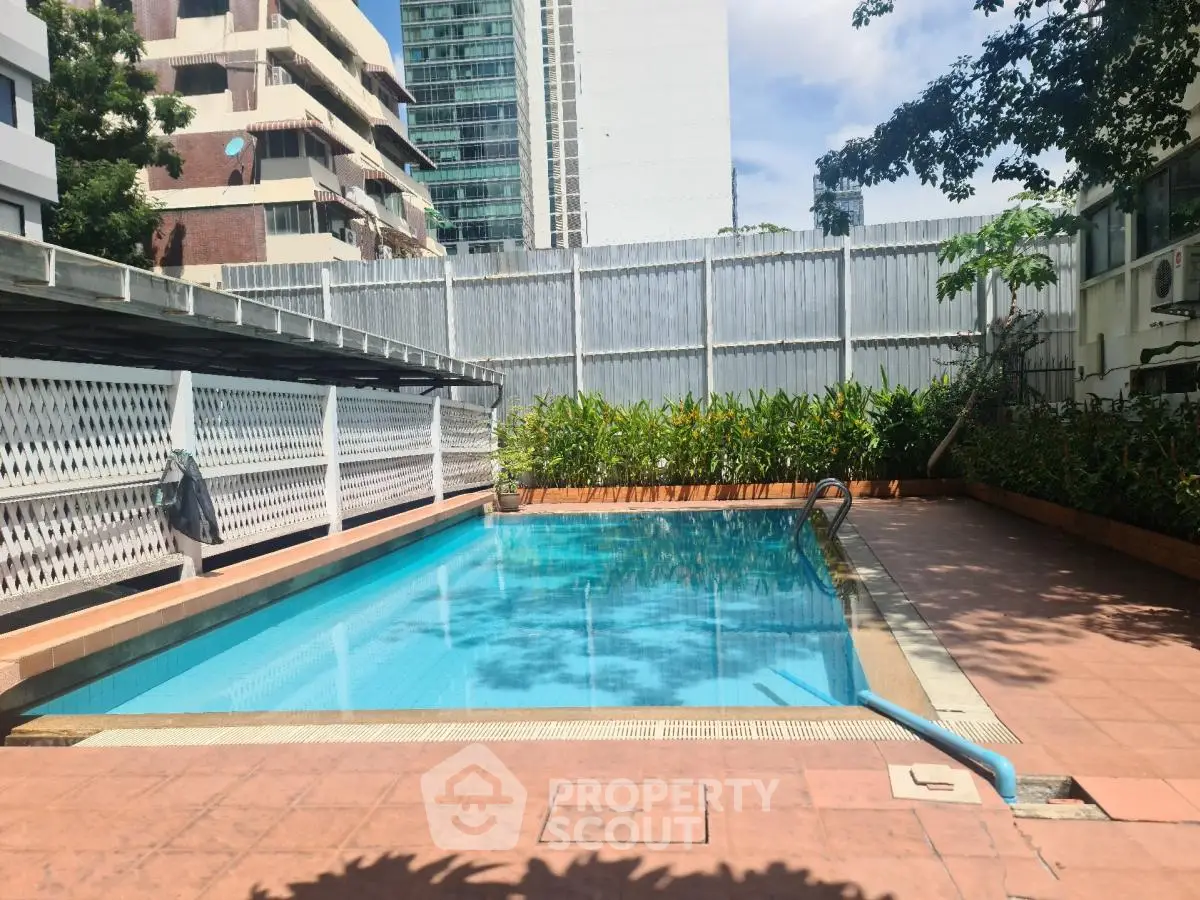 Inviting outdoor swimming pool in urban residential complex with lush greenery and modern architecture.