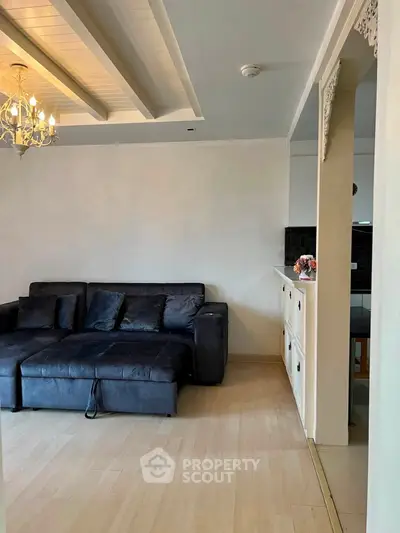 Spacious living room with elegant chandelier and cozy black sofa, perfect for relaxation and entertaining.