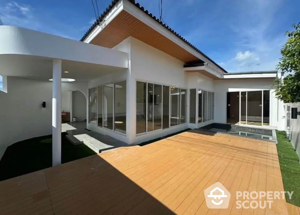 Modern white house with spacious wooden deck and large glass windows under clear blue sky.