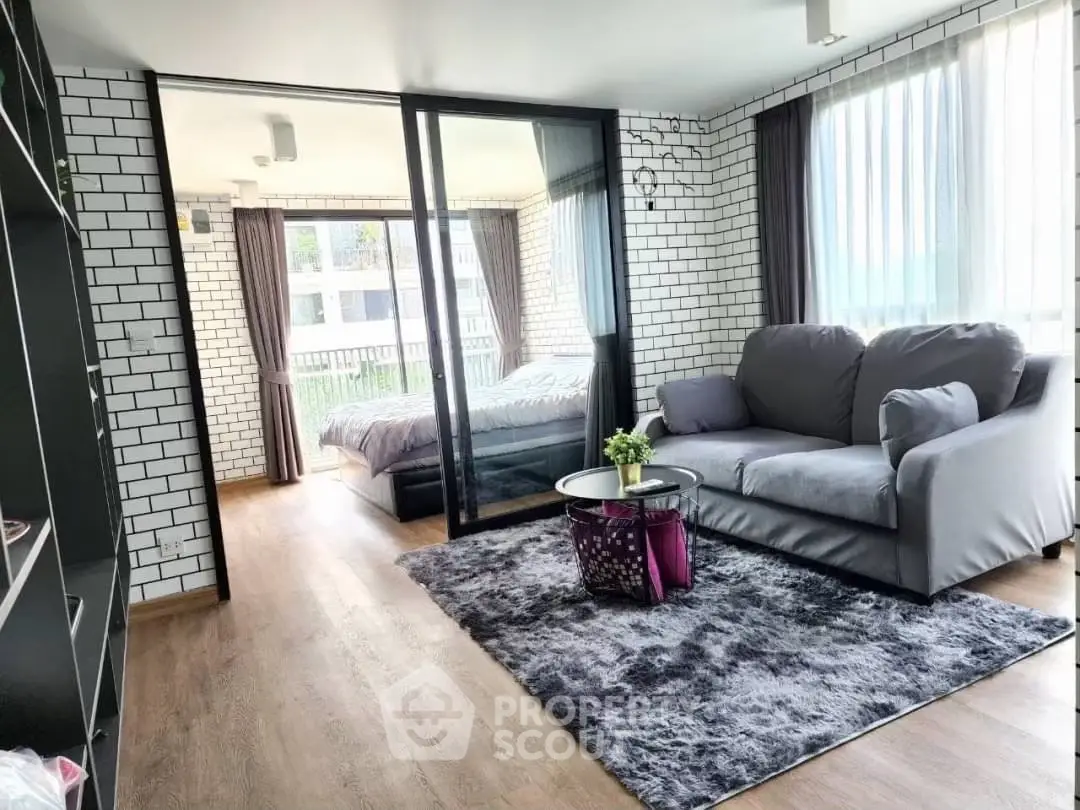 Modern living room with glass partition leading to a cozy bedroom, featuring stylish decor and natural light.