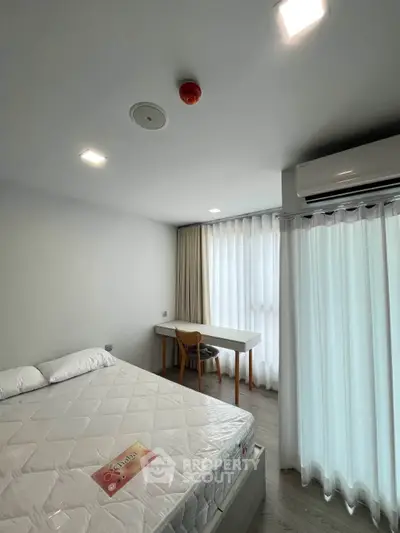 Modern bedroom with natural light, featuring a bed, desk, and air conditioning in a sleek apartment.