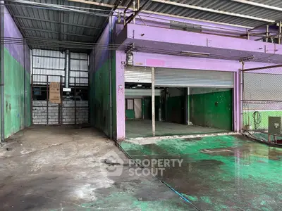 Spacious industrial warehouse with vibrant purple and green walls, featuring large open garage doors.