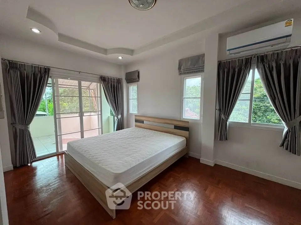 Spacious bedroom with large windows and balcony access, featuring elegant curtains and wooden flooring.