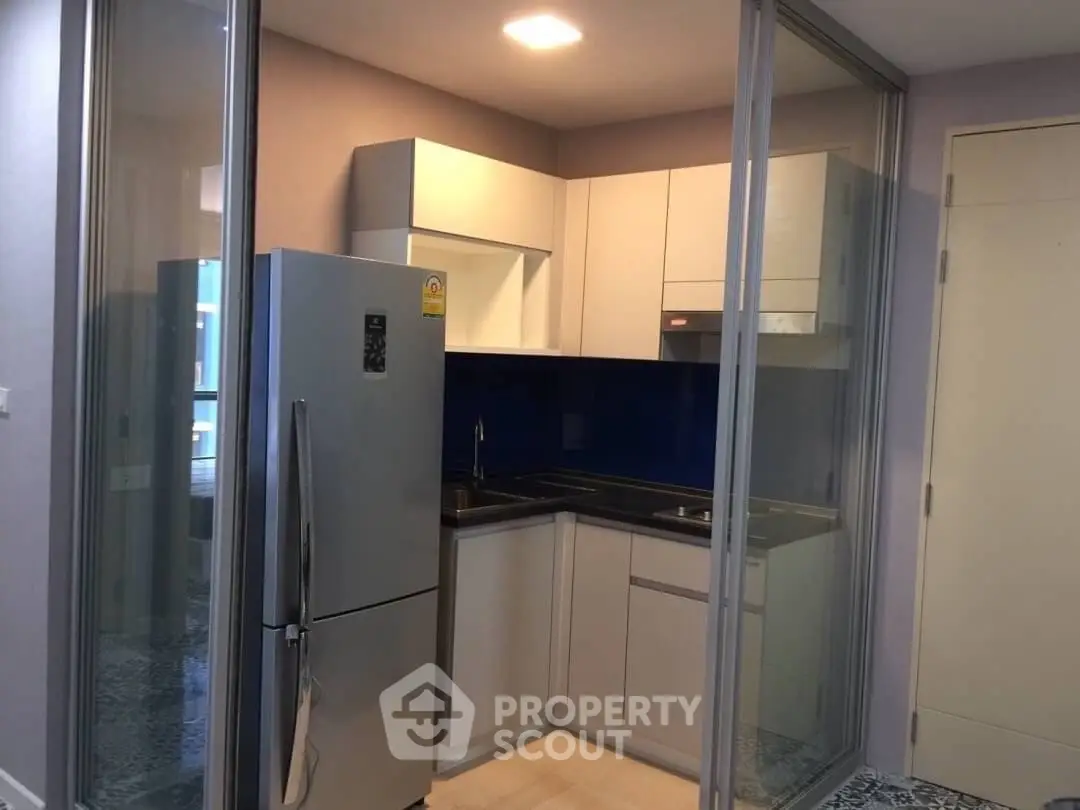 Modern compact kitchen with sleek cabinetry and stainless steel fridge in a cozy apartment.