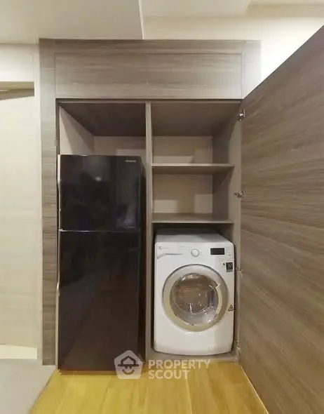 Compact laundry and storage area with washing machine and fridge in modern apartment.