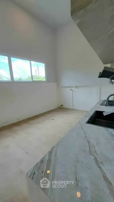 Spacious kitchen with modern marble countertops and large window for natural light.