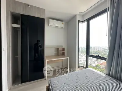 Modern bedroom with large windows and city view, featuring sleek wardrobe and compact desk.