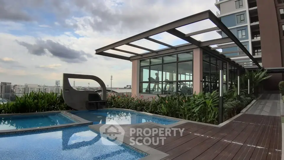 Modern rooftop pool with city view and glass-walled gym in luxury apartment complex.
