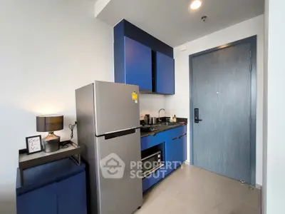 Modern compact kitchen with blue cabinets and stainless steel fridge in a stylish apartment.
