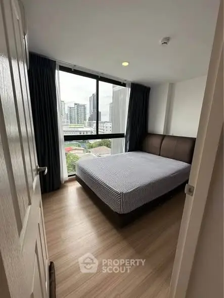 Modern bedroom with large window offering city view, featuring a comfortable bed and stylish decor.