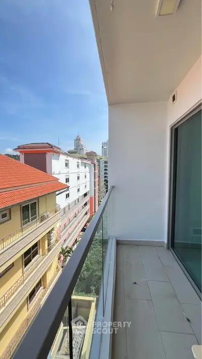 Modern balcony with glass railing offering city views and clear blue sky.