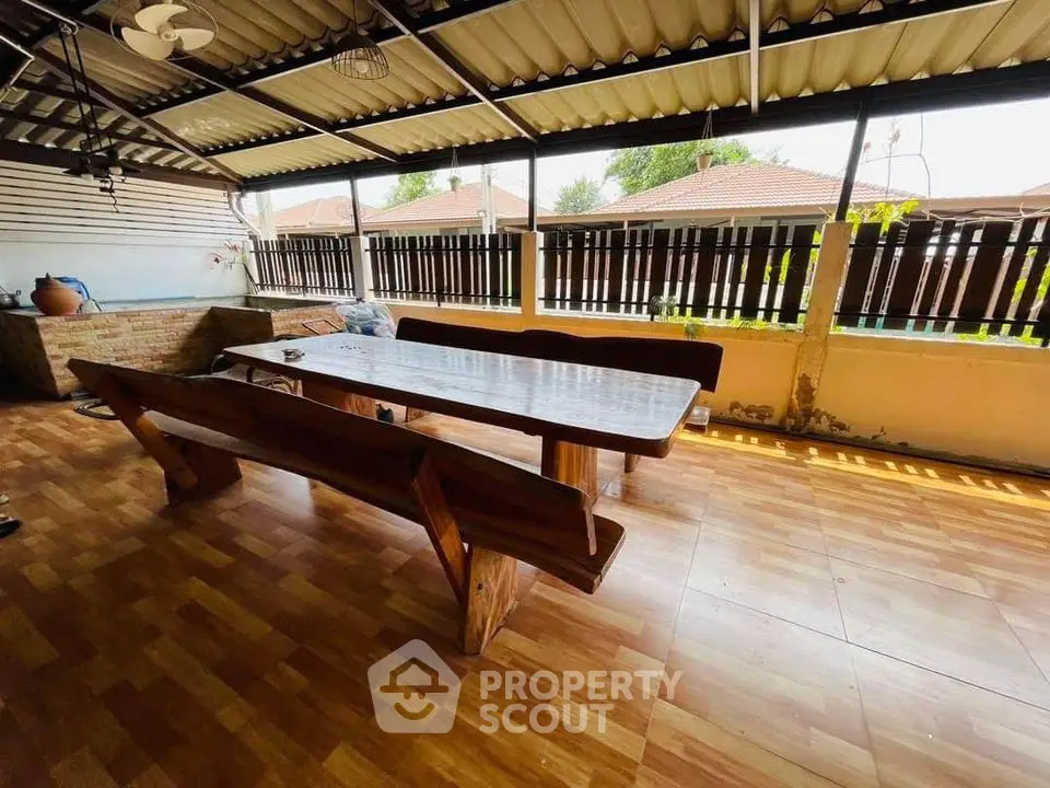 Spacious covered patio with wooden dining set and tiled flooring, perfect for outdoor gatherings.