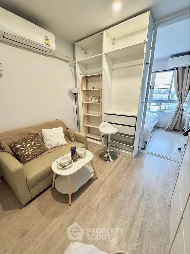 Cozy living room with modern decor and open view to bedroom, featuring a compact sofa and stylish shelving.