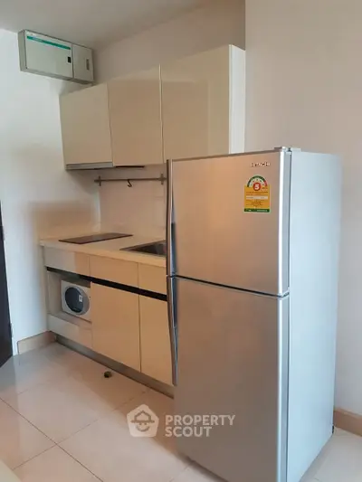 Modern kitchen with sleek cabinets, fridge, and washing machine in compact layout.