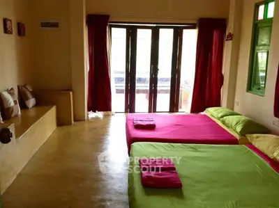 Spacious bedroom with vibrant bedding and natural light from large windows.