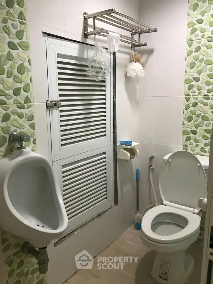 Compact bathroom with urinal and toilet, featuring green leaf-patterned tiles and white fixtures.