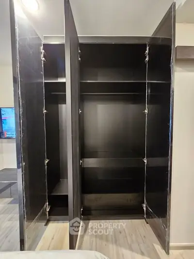 Spacious black wardrobe with open doors showcasing ample storage space in modern bedroom.