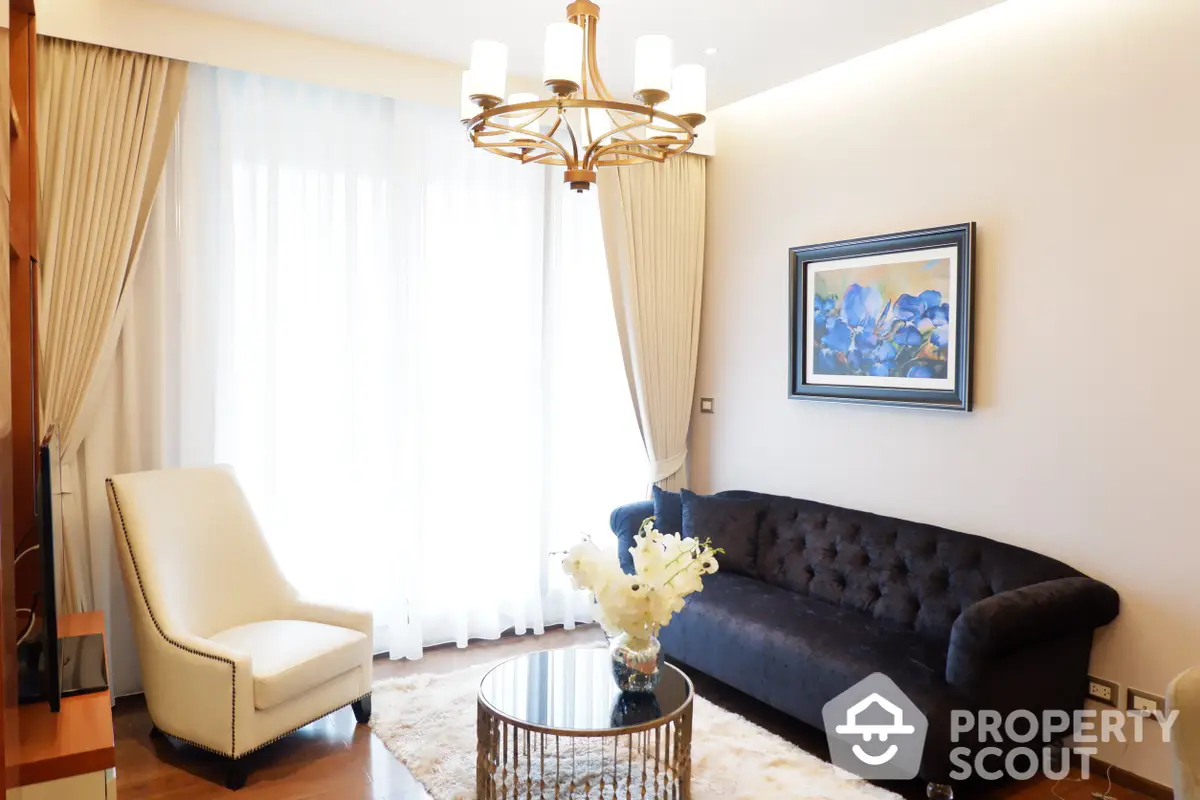 Elegant living room with polished hardwood floors, a plush navy sofa, and a chic chandelier creating a warm, inviting atmosphere.