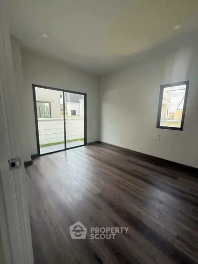 Spacious room with dark wood flooring and large window, perfect for natural light.
