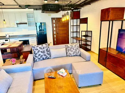 Modern living room with stylish furniture and open kitchen layout, featuring a cozy gray sofa and wooden accents.