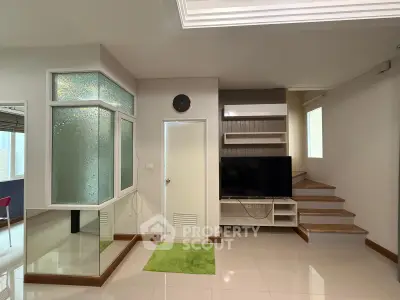Modern living room with sleek staircase and built-in TV unit, featuring stylish frosted glass accents.
