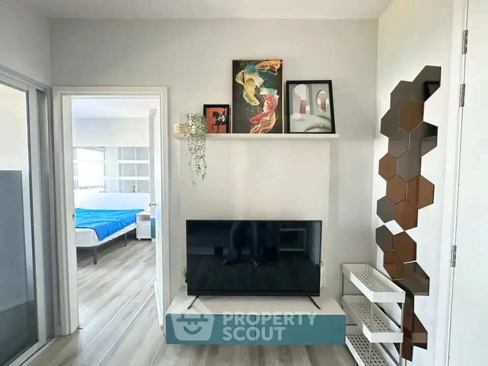 Modern living room with stylish decor and view into a cozy bedroom, featuring a sleek TV setup and artistic wall accents.