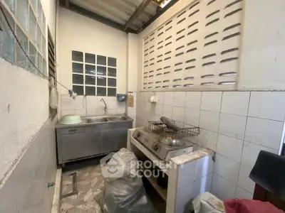 Compact kitchen with stainless steel sink and gas stove, featuring tiled walls and a rustic design.