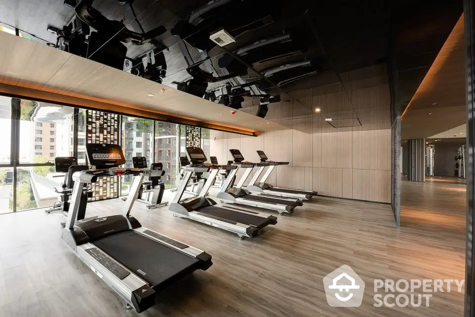 Modern gym with multiple treadmills and large windows in luxury apartment complex.