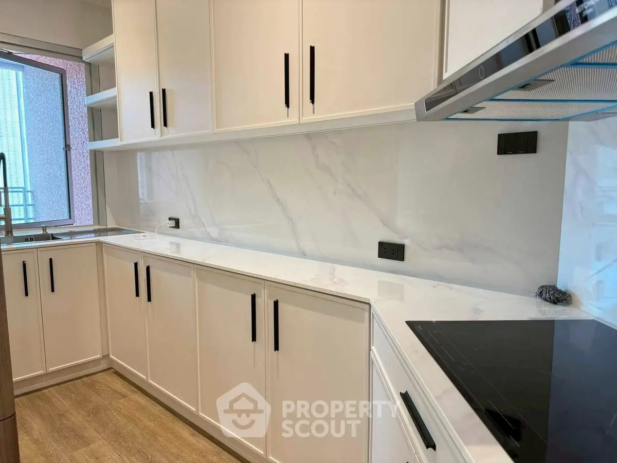 Modern kitchen with sleek white cabinets and marble backsplash, featuring an induction cooktop and ample counter space.