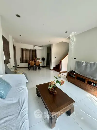 Spacious living room with modern decor and natural light, featuring a cozy seating area and elegant dining space.