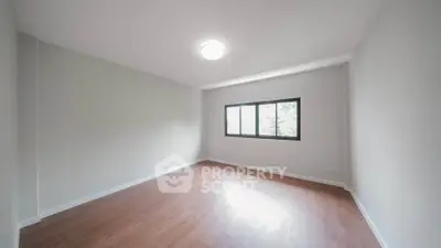 Spacious empty room with wooden flooring and large window, perfect for customization.