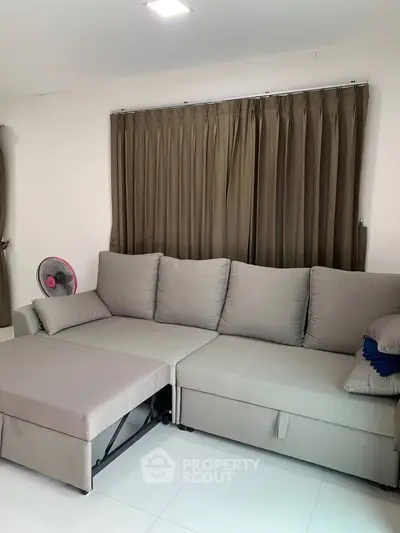 Spacious living room with modern gray sectional sofa and elegant curtains, perfect for relaxation.