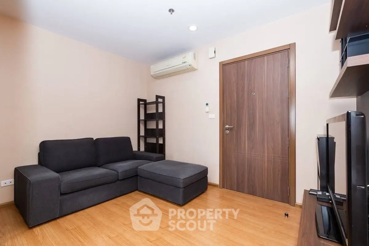 Modern living room with sleek black sofa and wooden flooring, featuring a minimalist design and air conditioning.