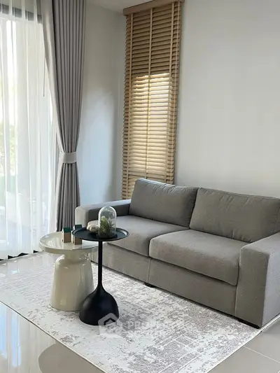 Modern living room with sleek gray sofa and stylish decor, featuring large windows and elegant curtains.