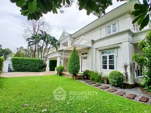 Charming white house with lush green garden and elegant entrance.