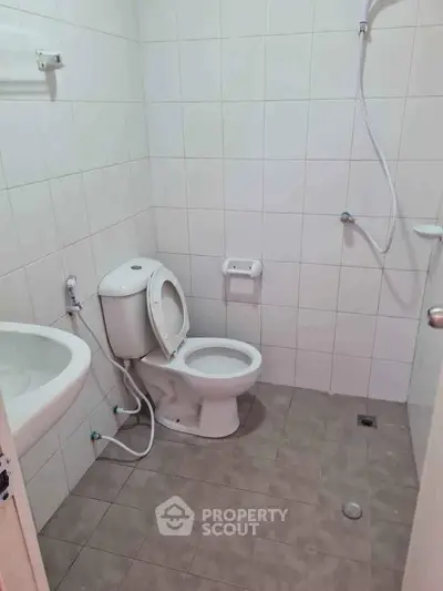Compact bathroom with shower, toilet, and sink in a tiled setting.