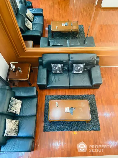 Spacious living room with polished hardwood floors and comfortable black leather sofas, accented by a classic wooden coffee table.