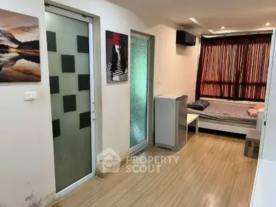 Cozy bedroom with modern decor and natural light, featuring a small fridge and stylish artwork.